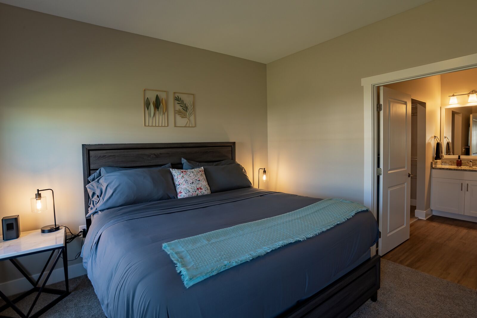Quarto com uma cama grande, luminárias de cabeceira, mesa de cabeceira e porta para um banheiro.