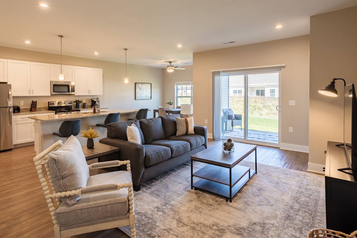 A modern living room with a sofa, armchair, coffee table, and a kitchen in the background.