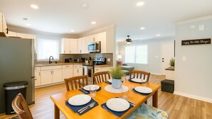 Une cuisine moderne avec des meubles blancs, un îlot central et un coin repas doté d’une table en bois, mise pour quatre personnes.