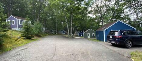 A row of small, single-story cabins with a paved driveway leading to them, surrounded by trees.