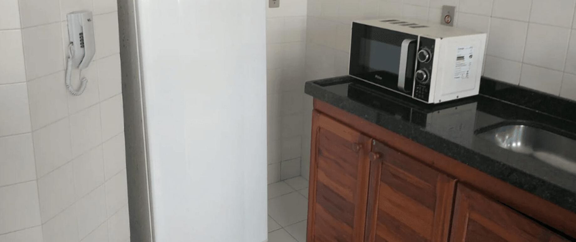 A kitchen with a microwave on a black countertop, wooden cabinets, and a white tiled backsplash.