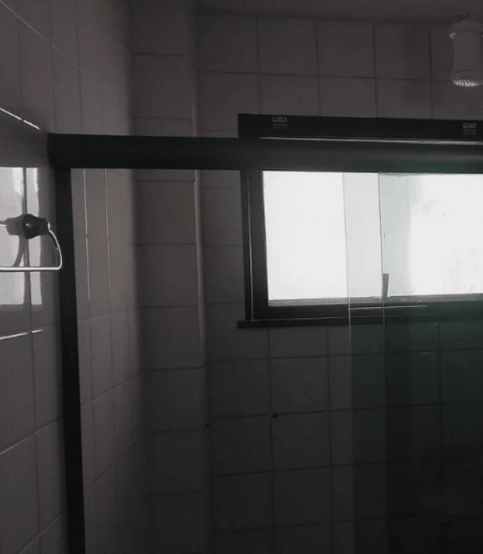 A bathroom with white tiles, a window, and a shower area.