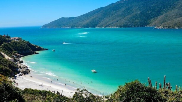 A coastal landscape with a beach, clear turquoise waters, and a mountainous backdrop. - Arraial do Cabo - Prainha (Arraial do Cabo)