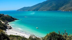 A coastal landscape with a beach, clear turquoise waters, and a mountainous backdrop. - Arraial do Cabo - Prainha (Arraial do Cabo)
