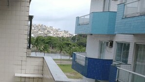 A building with a tiled exterior, a visible window, and a view of a residential area with houses and greenery in the background. - Arraial do Cabo - Prainha (Arraial do Cabo)