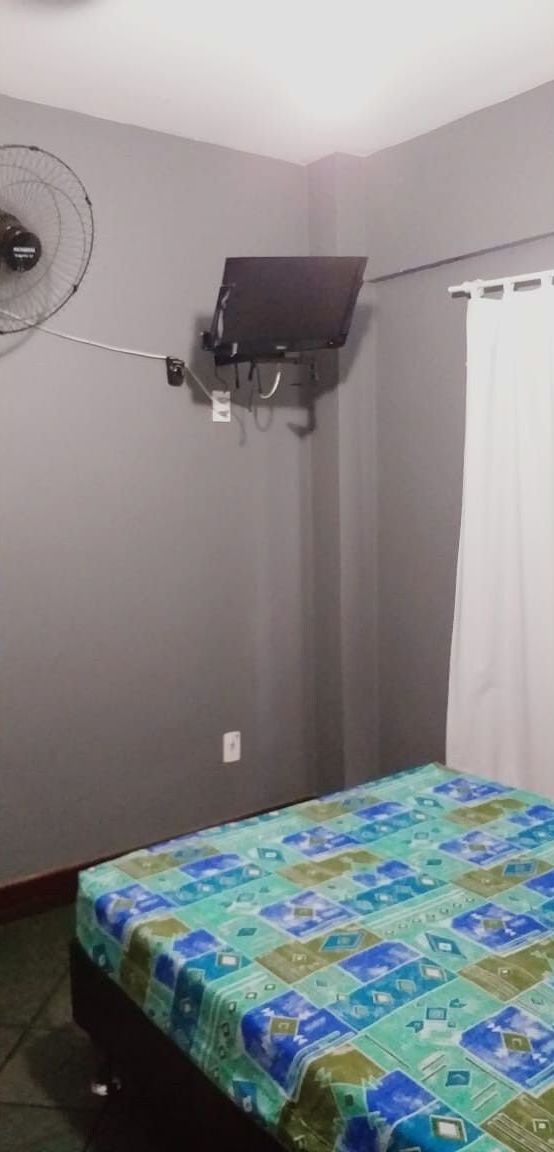 A room with a bed, a wall-mounted TV, and a ceiling fan.