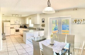 A modern kitchen with white cabinets, a central island, and a dining area with a table and chairs.