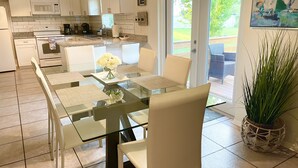 Una cocina moderna con armarios blancos, una mesa de comedor de vidrio y una planta en maceta.