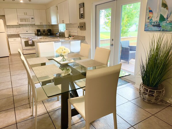 Une cuisine moderne avec des meubles blancs, une table à manger en verre et une plante en pot.