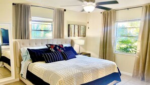 Un dormitorio con cama, cortinas, ventilador de techo, ventana y un cuadro en la pared.