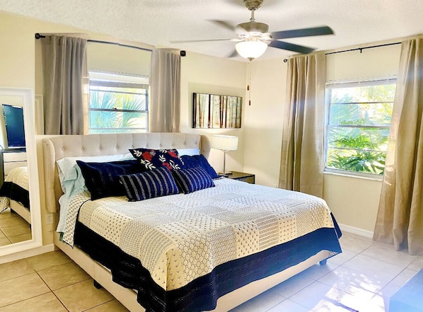 A bedroom with a bed, curtains, a ceiling fan, a window, and a painting on the wall.