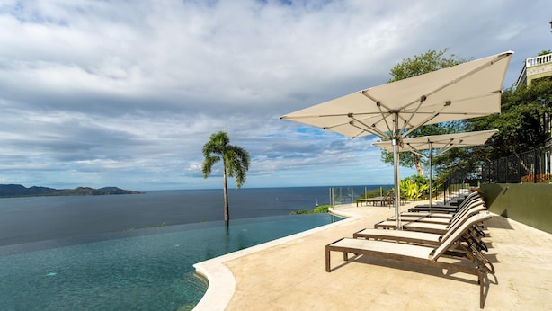 An infinity pool with clear water, a palm tree, and lounge chairs with umbrellas. - 360 Splendor 403-Condo with Breakfast Included (360 Splendor)