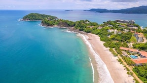 An aerial view of a coastal area with a beach, a small island, and a resort with multiple buildings. - 360 Splendor 403-Condo with Breakfast Included (360 Splendor)