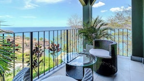 A balcony with a glass table and wicker furniture, overlooking a coastal landscape with a clear sky. - 360 Splendor 403-Condo with Breakfast Included (360 Splendor)