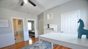 A spacious living room with hardwood floors, a white table, and a blue rug. There is a white door and a ceiling fan.