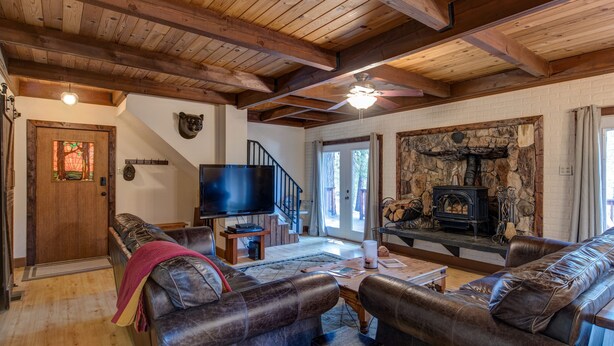Una sala de estar acogedora con sofás de cuero, chimenea, televisor y techo de madera.