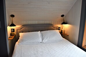 A bedroom with a wooden headboard, white bedding, and two bedside lamps.