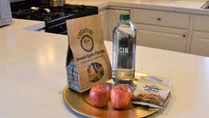 En köksbänk med en påse chips, en flaska gin, äpplen och ett paket kakor. Ett välkomstkort ligger synligt.