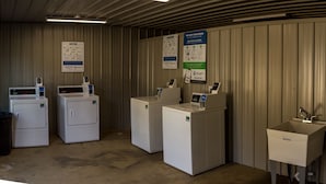 Un cuarto de lavandería con tres lavadoras, un lavamanos y carteles informativos sobre las máquinas.