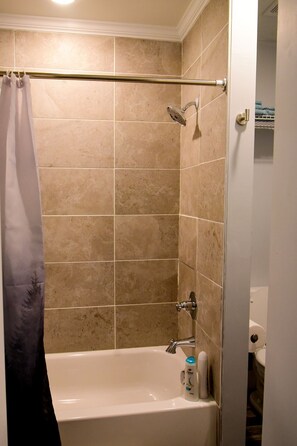 A bathroom with beige tiles, a bathtub, a shower, and a towel rack. - Coleman Park Studios (Iuka)