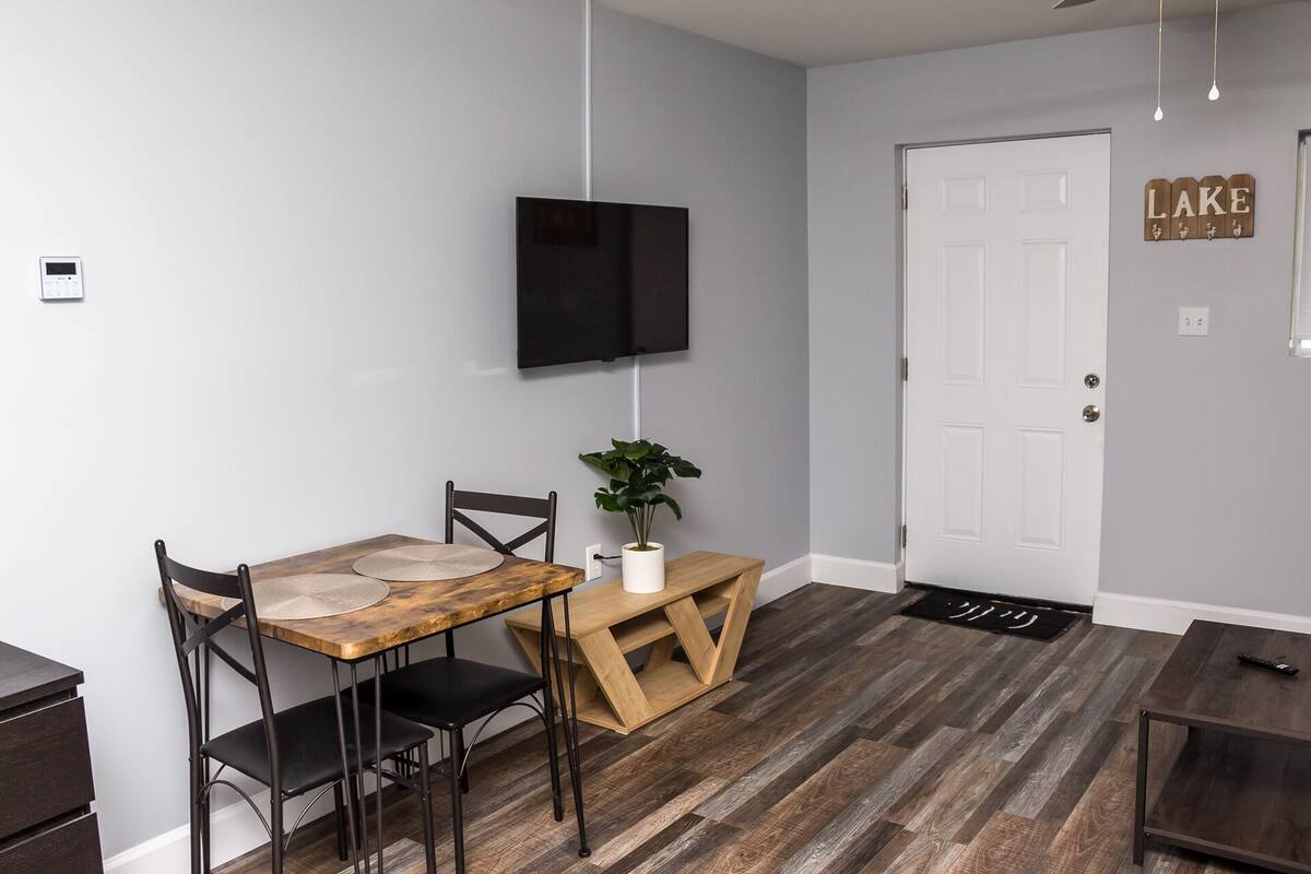 A dining area with a wooden table, two chairs, a potted plant, and a TV mounted on the wall.