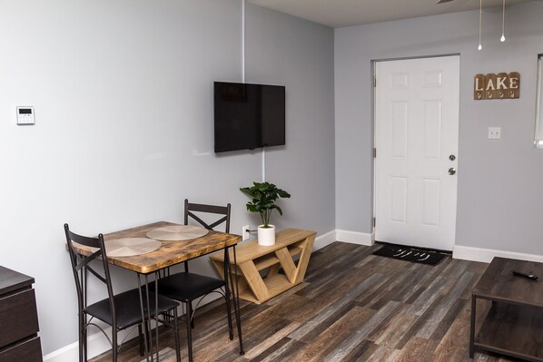 A dining area with a wooden table, two chairs, a potted plant, and a TV mounted on the wall. - Coleman Park Studios (Iuka)