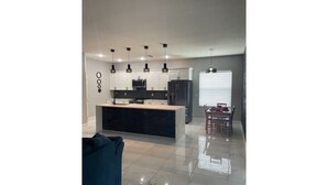 Una cocina moderna con una isla central, iluminación colgante y un comedor con sillas y una mesa.