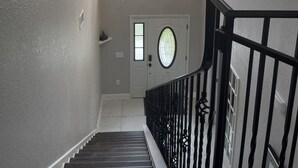 Una escalera con barandal negro, un candelabro y una puerta con ventanal.
