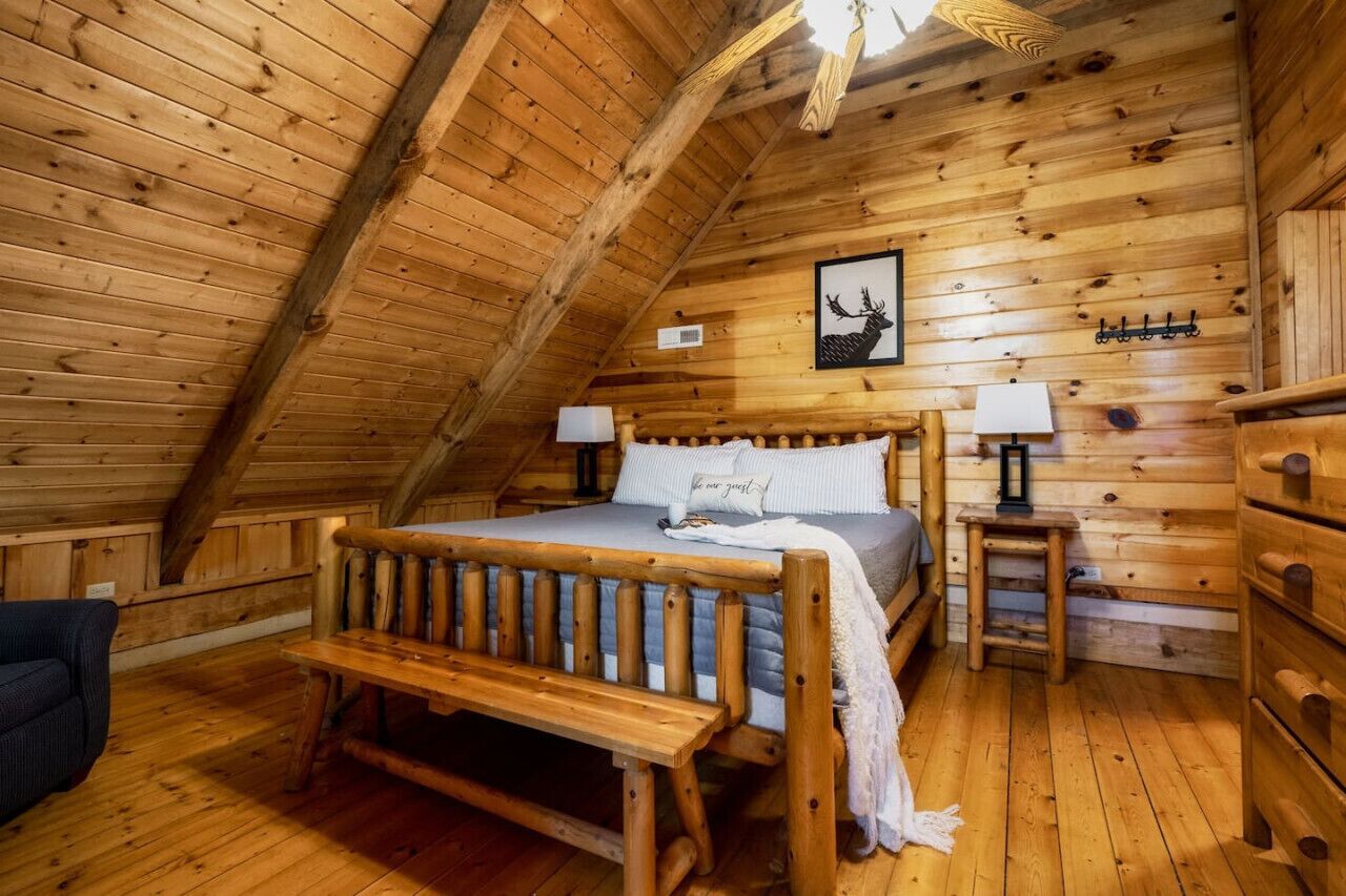 A wooden cabin bedroom with a loft bed, two bedside tables, a bench, and a wooden dresser.