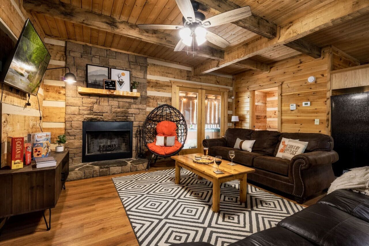 Ein gemütliches Blockhaus-Interieur mit Kamin, Holzbalkendecke, einer bequemen Couch und einem an der Wand befestigten Fernseher.