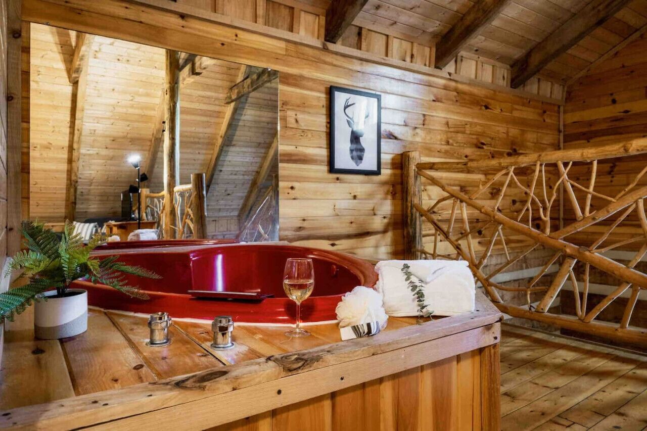 A wooden cabin interior with a red bathtub, a mirror, a framed deer head, and a wooden ladder.