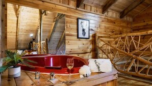 Ein Holzhütten-Interieur mit einer roten Badewanne, einem Spiegel, einem Hirschgeweihbild und einer Holzleiter.
