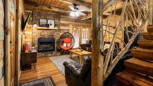 Ein rustikales Interieur mit Kamin aus Stein, Holzboden und einer schwarzen Ledersofa sowie einer Holztreppe.