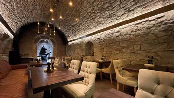 Un restaurante con paredes de piedra y un techo alto, que incluye una mesa de madera y sillas con cojines.