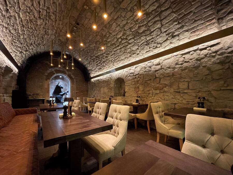 Un restaurante con paredes de piedra y un techo alto, que incluye una mesa de madera y sillas con cojines.