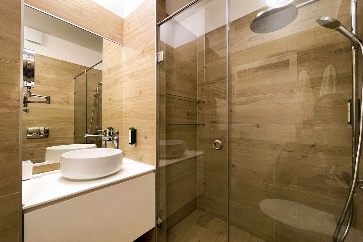 A modern bathroom with a glass-enclosed shower, a white sink, and a large mirror.