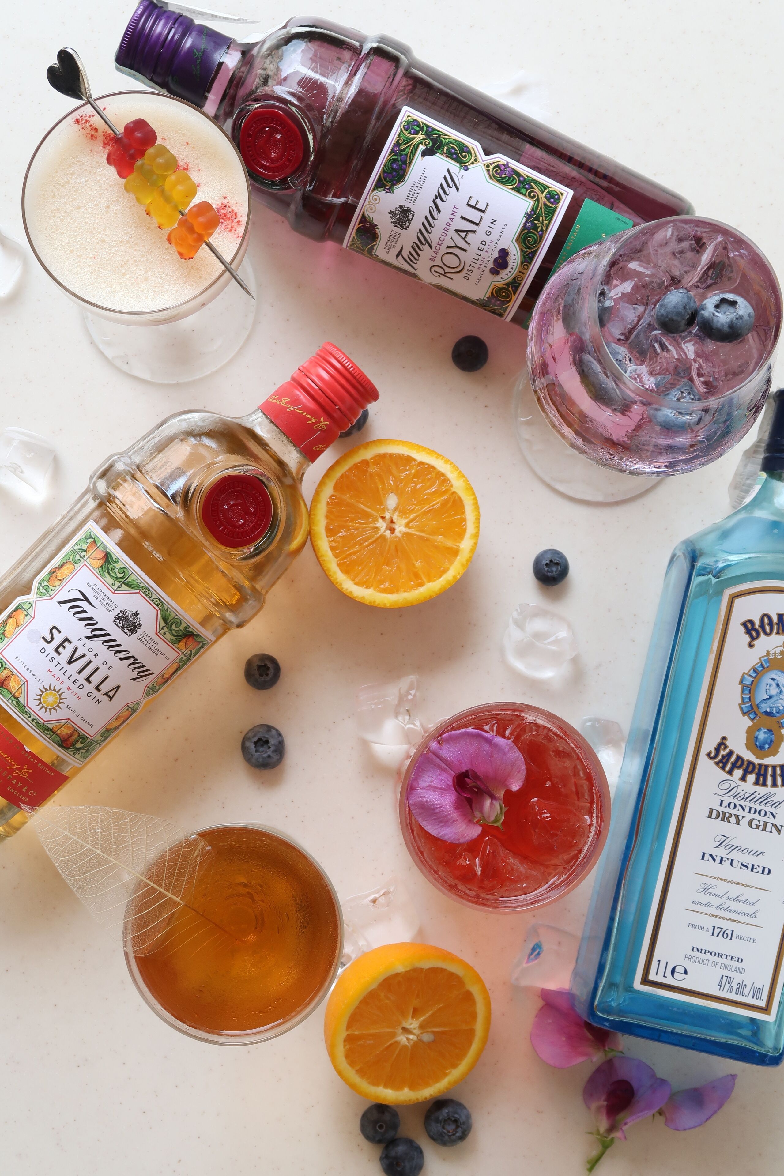 Variedad de bebidas y botellas sobre una mesa, incluyendo una botella de ginebra de Sevilla, una botella de ginebra London Dry y una botella de ginebra Bombay Sapphire.