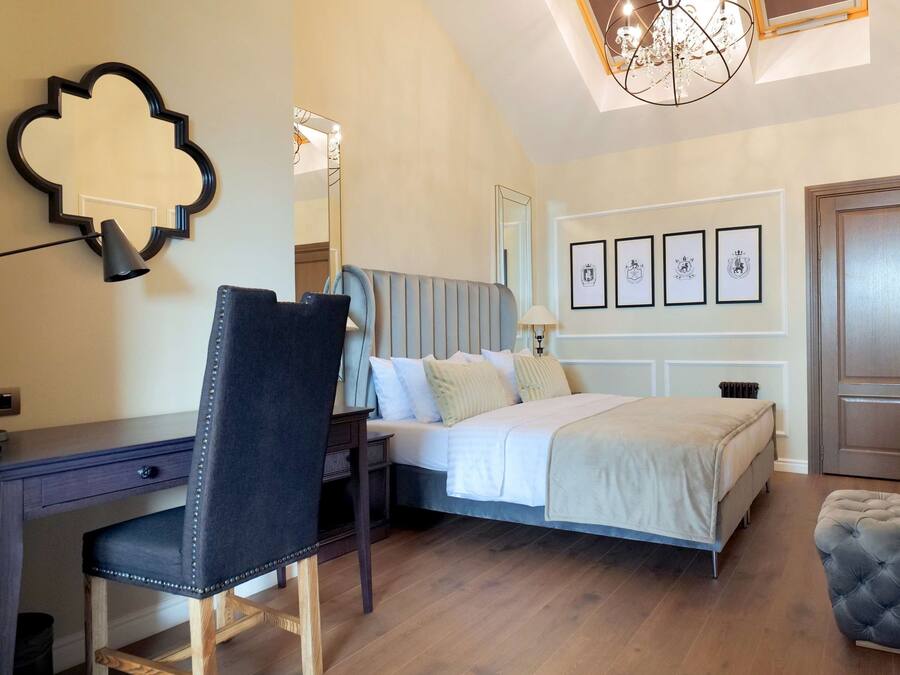 A bedroom with a bed, a desk, a chair, a large mirror, and a chandelier.