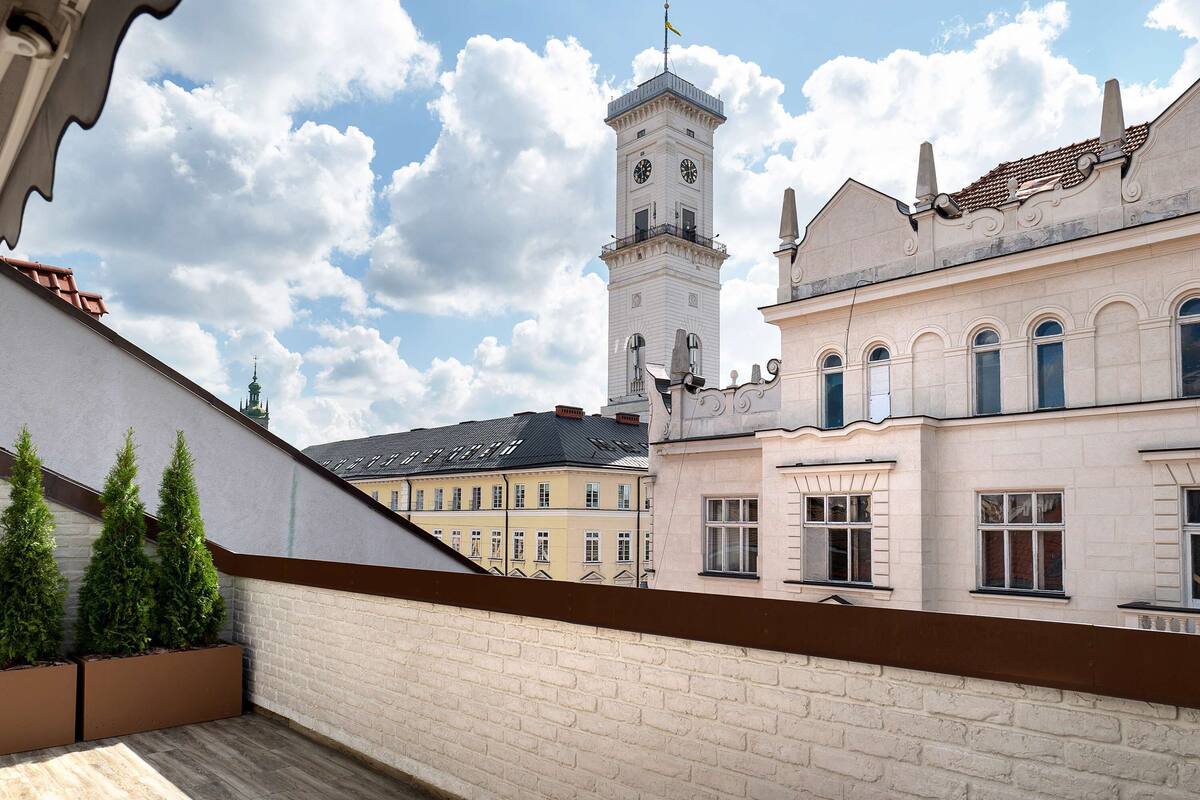 A balcony with a view of a historic building with a clock tower, brick walls, and a clear sky.