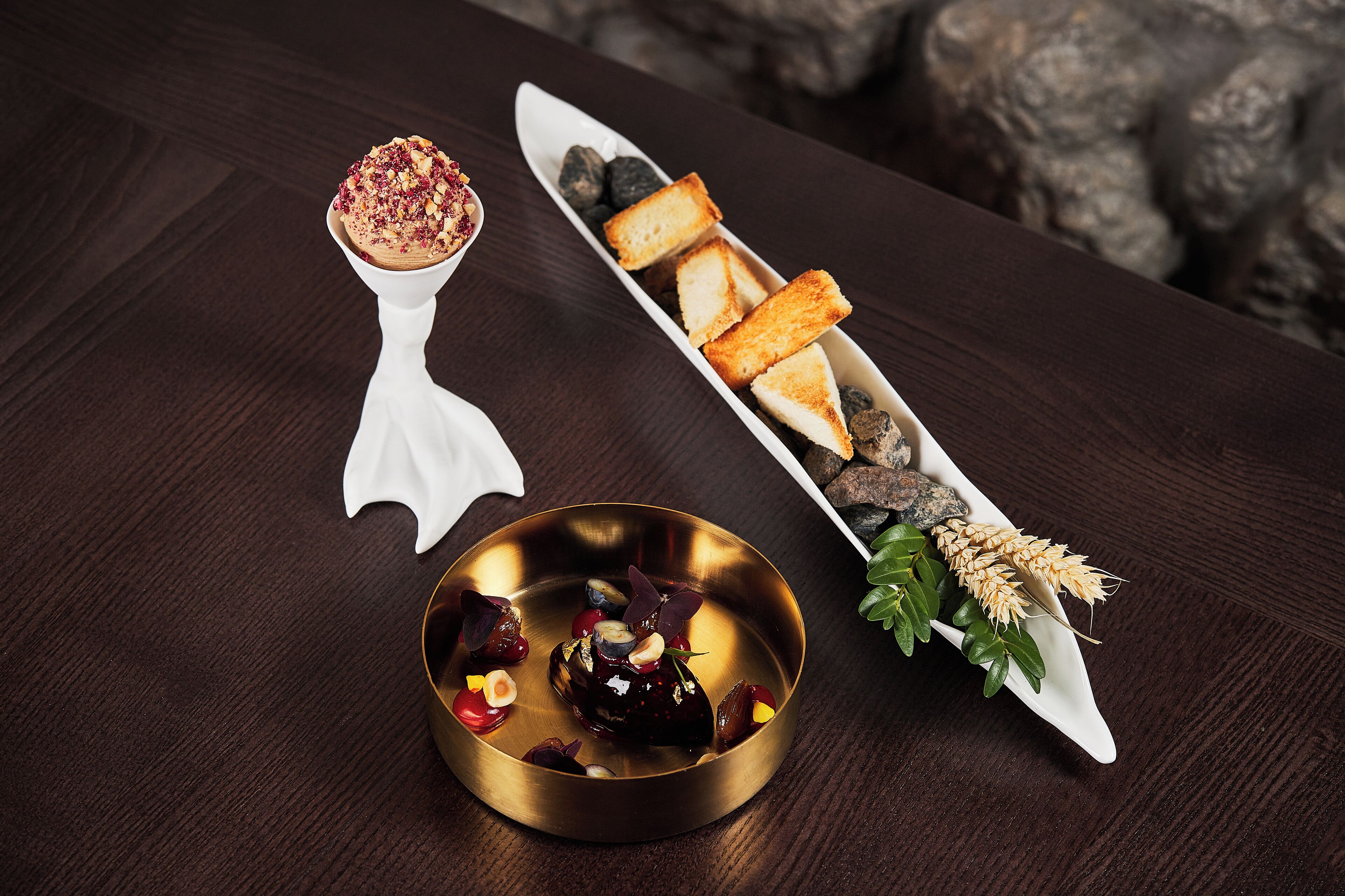 A dessert plate with a golden bowl, a white dessert spoon, and a white serving dish with bread and berries.