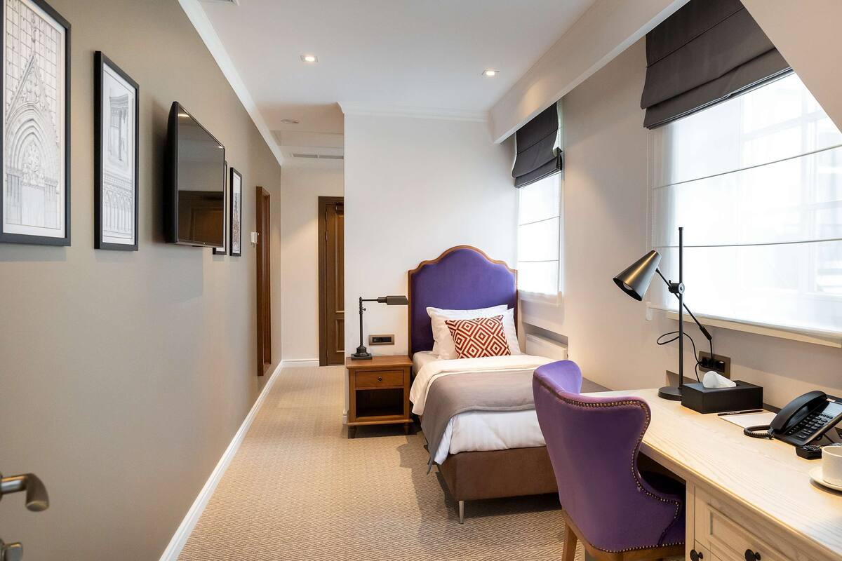 A hotel room with a bed, desk, chair, and a window with blinds.