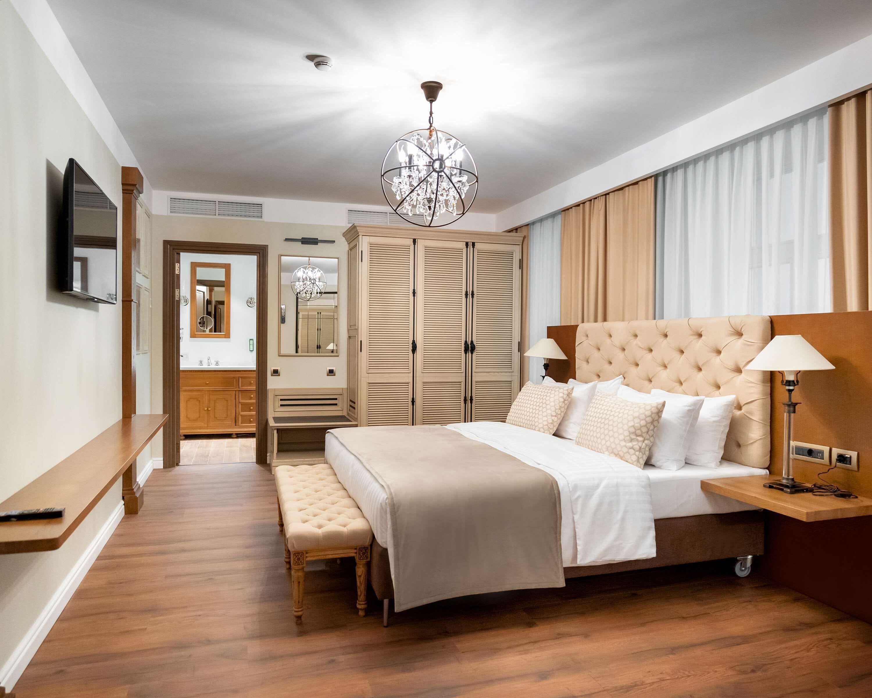 Une chambre à coucher avec un grand lit, un banc, une armoire, un miroir et un lustre.