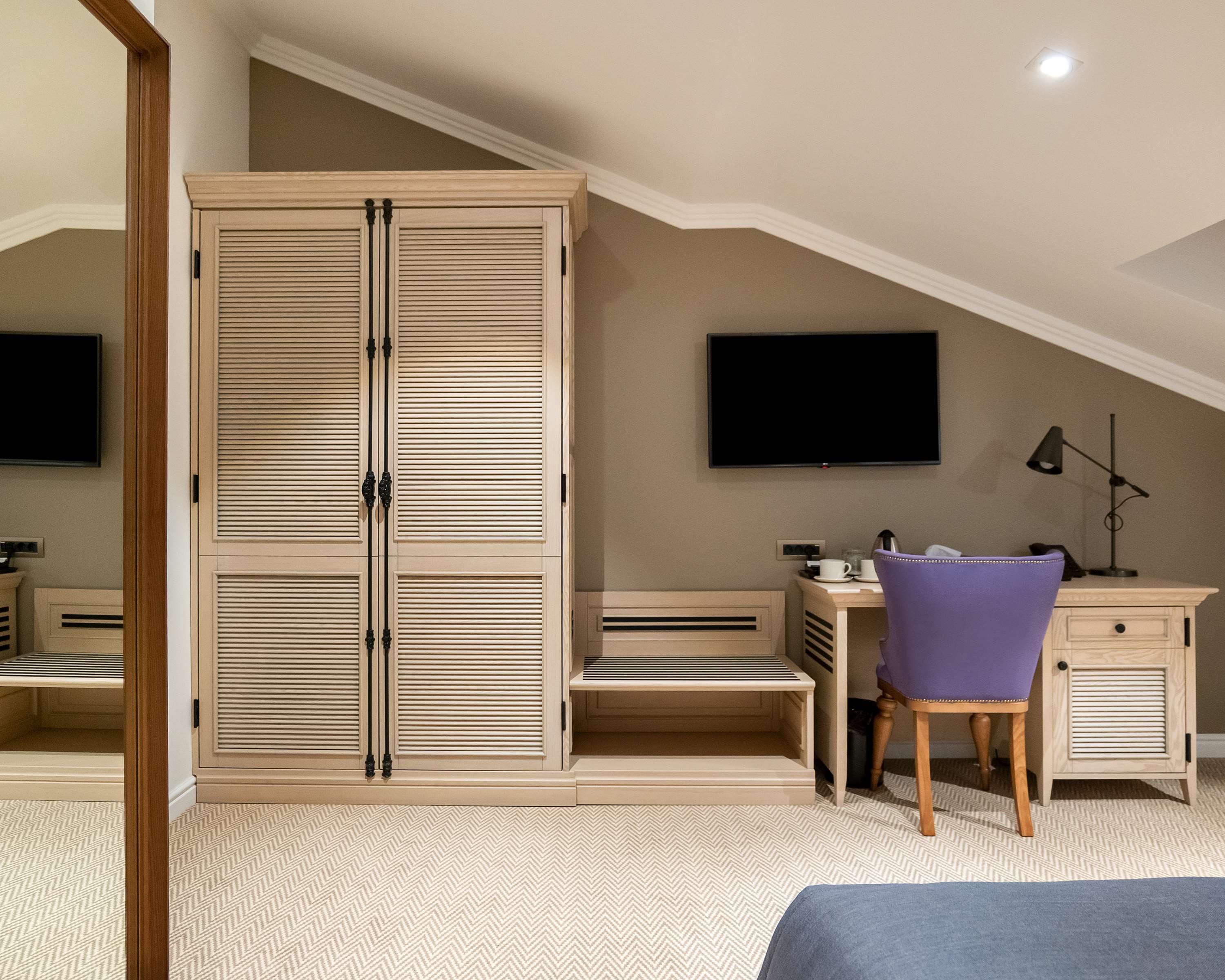 A bedroom with a large wardrobe, a desk with a chair, a television, and a lamp.