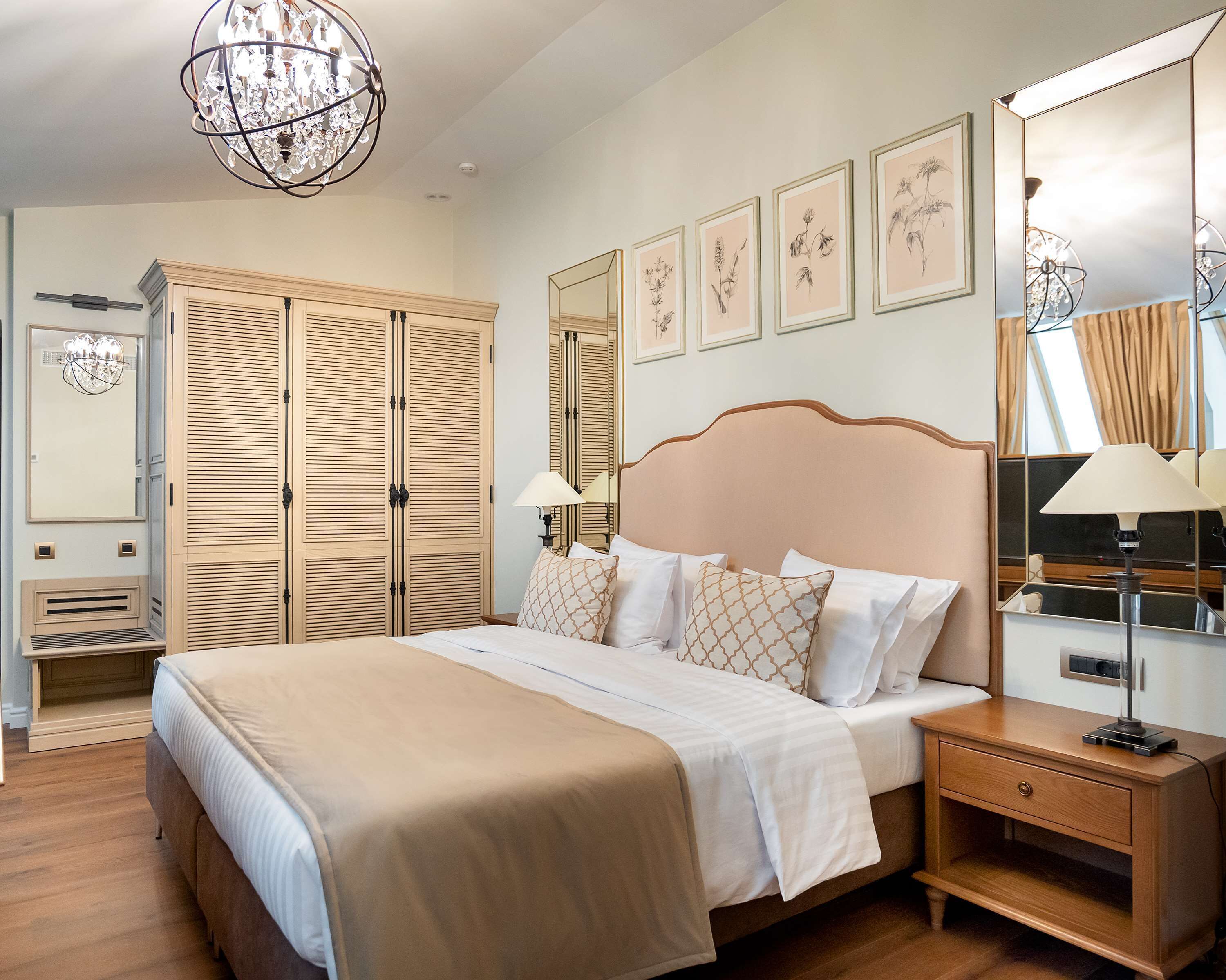 A neatly arranged bedroom with a large bed, wooden wardrobe, and framed botanical prints on the wall.