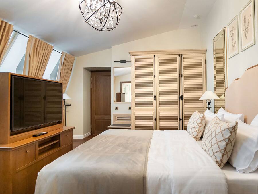 Una habitación de hotel con una cama grande, televisión, armario y candelabro.