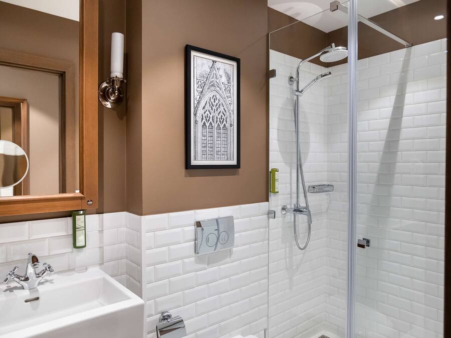 A bathroom with a sink, mirror, framed artwork, and a glass-enclosed shower area.