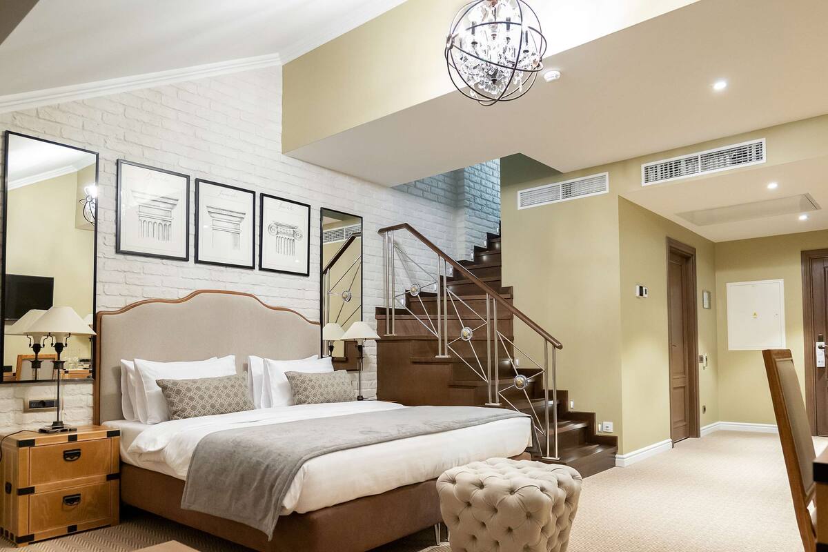A modern bedroom with a large bed, a wooden bench, a staircase, and framed artwork on the wall.