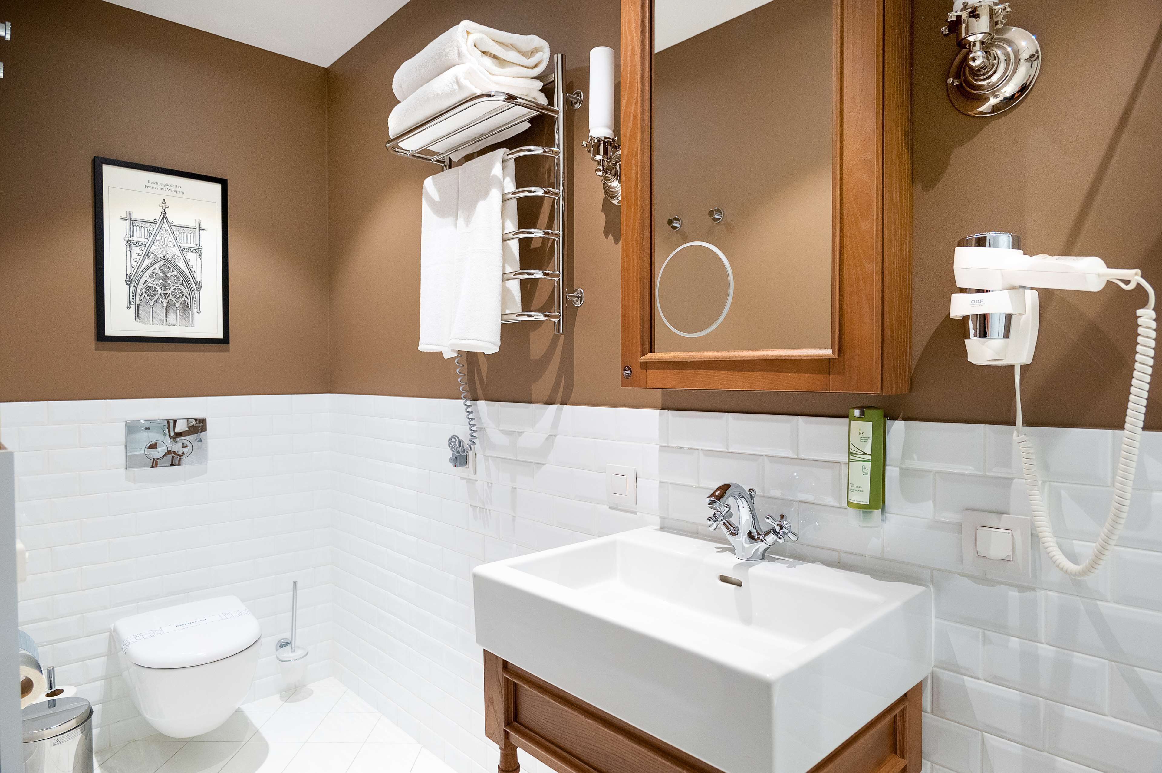 A bathroom with a white sink, a toilet, a towel rack, a framed picture on the wall, and a hairdryer mounted on the wall.