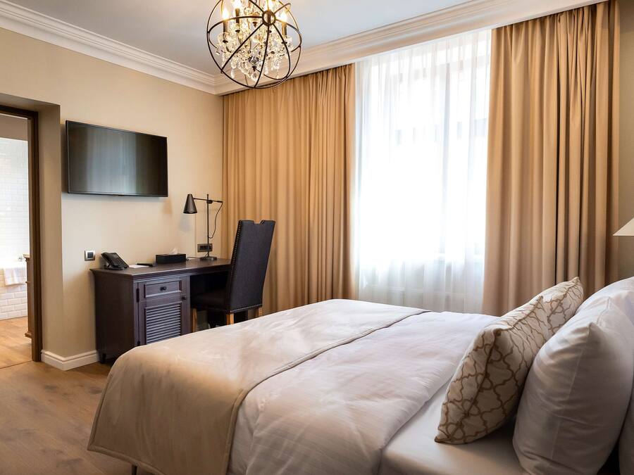 Une chambre d’hôtel avec un lit, un bureau et une chaise, une télévision et un lustre.