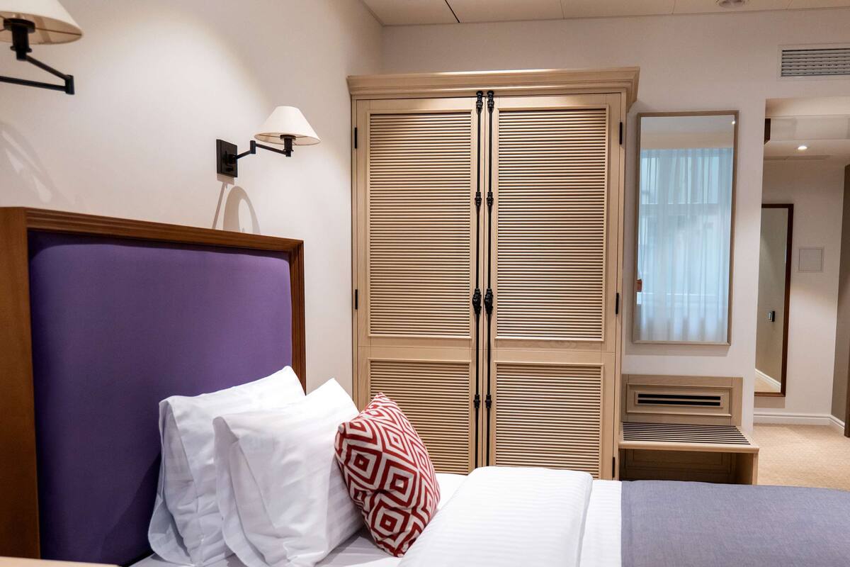 A hotel room with a bed, a wardrobe, a nightstand, and a mirror.